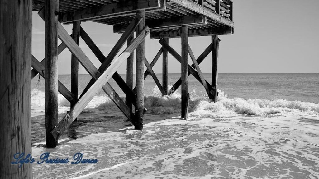 Black and white side view of waves crashing into a pier.