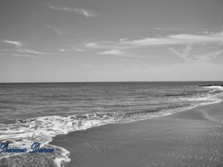 Black and white of waves rolling onto the shore. A few passing clouds above.