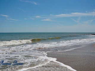 Waves crashing into the shore of Edisto Beach. A few passing clouds above.