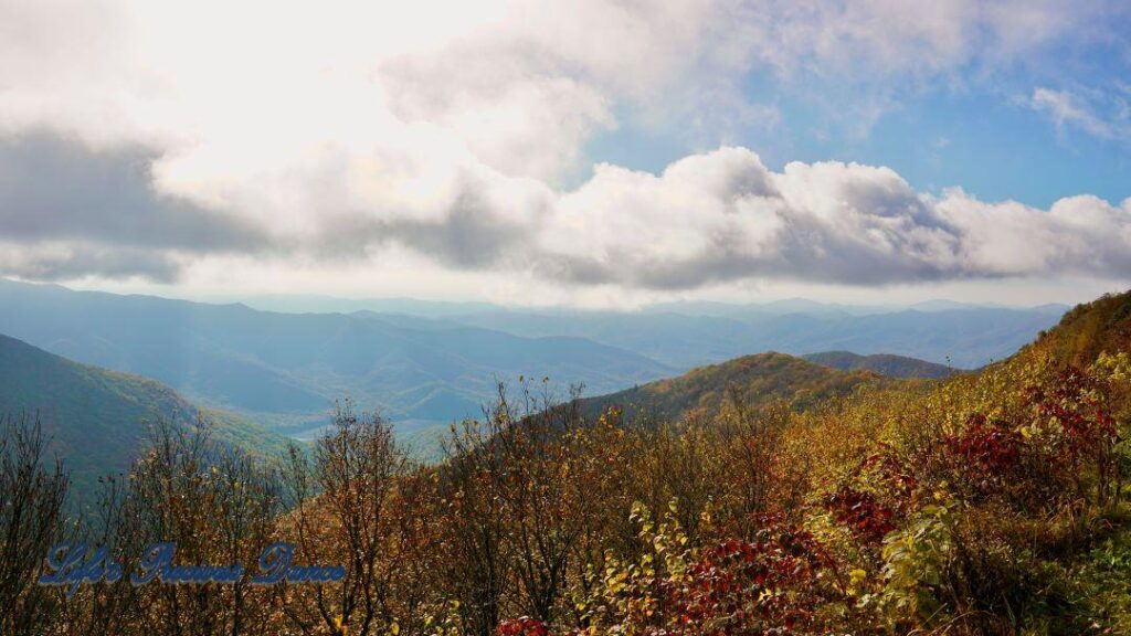 Landscape view of the colorful trees of the Blue Ridge Mountains. Passing clouds against a Carolina blue sky and fog in the valley.