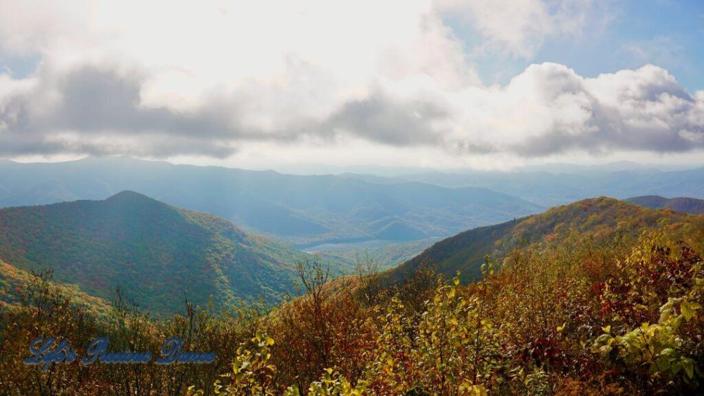 Landscape view of the colorful trees of the Blue Ridge Mountains. Passing clouds against a Carolina blue sky and fog in the valley.