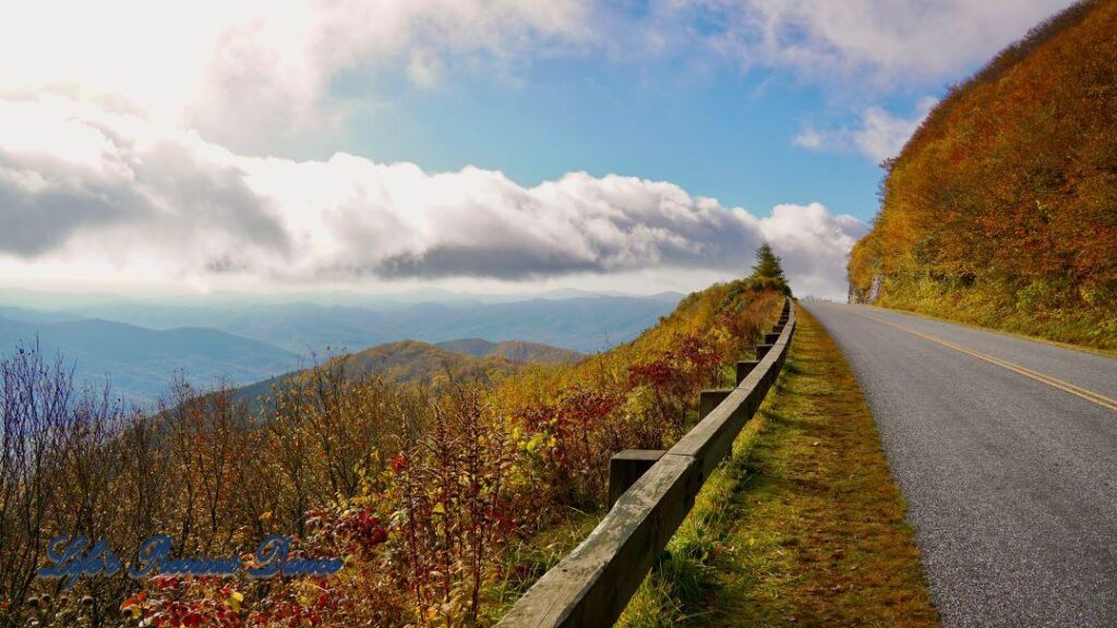 Landscape view of the colorful trees of the Blue Ridge Mountains. Passing clouds against a Carolina blue sky and the parkway to the right.