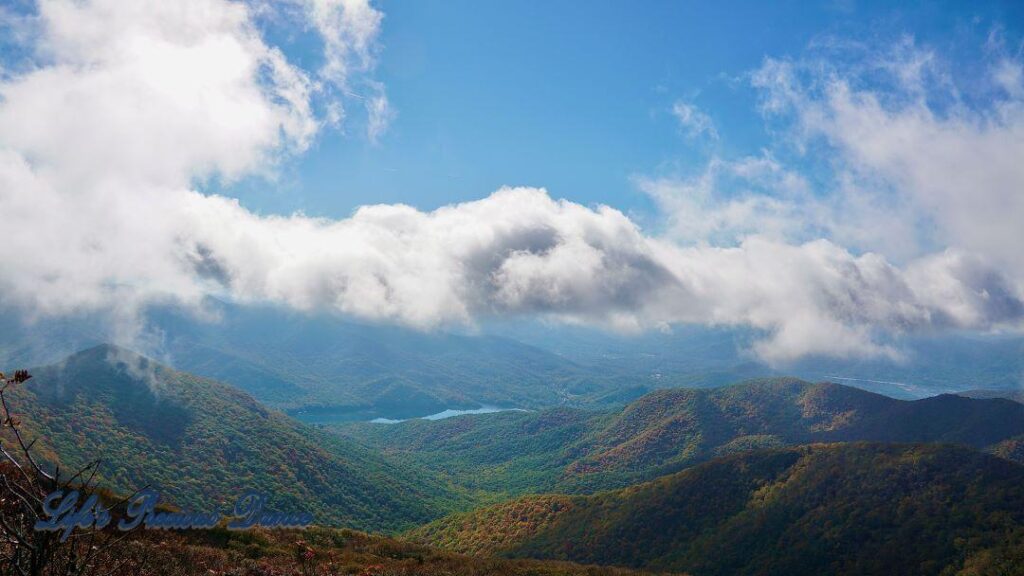 Landscape view of colorful trees, in the Blueridge mountains, surrounding a lake in the valley. Fluffy clouds above.