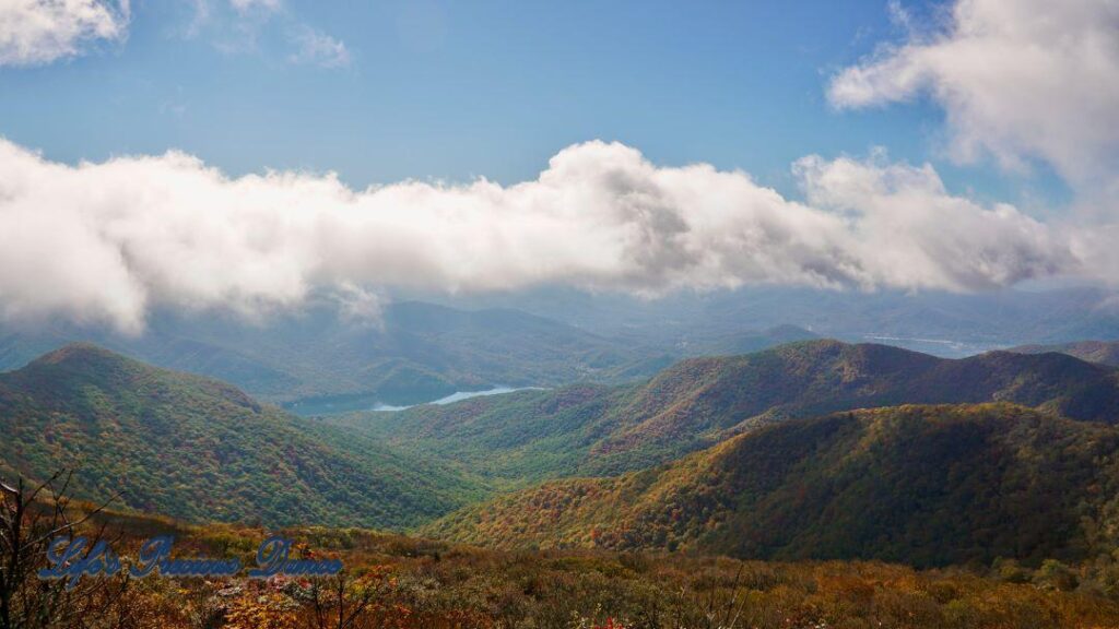 Landscape view of colorful trees, in the Blueridge mountains, surrounding a lake in the valley. Fluffy clouds above.