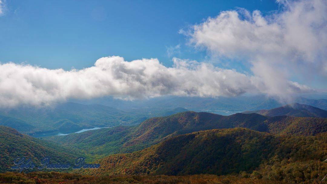 Landscape view of colorful trees, in the Blueridge mountains, surrounding a lake in the valley. Fluffy clouds above.