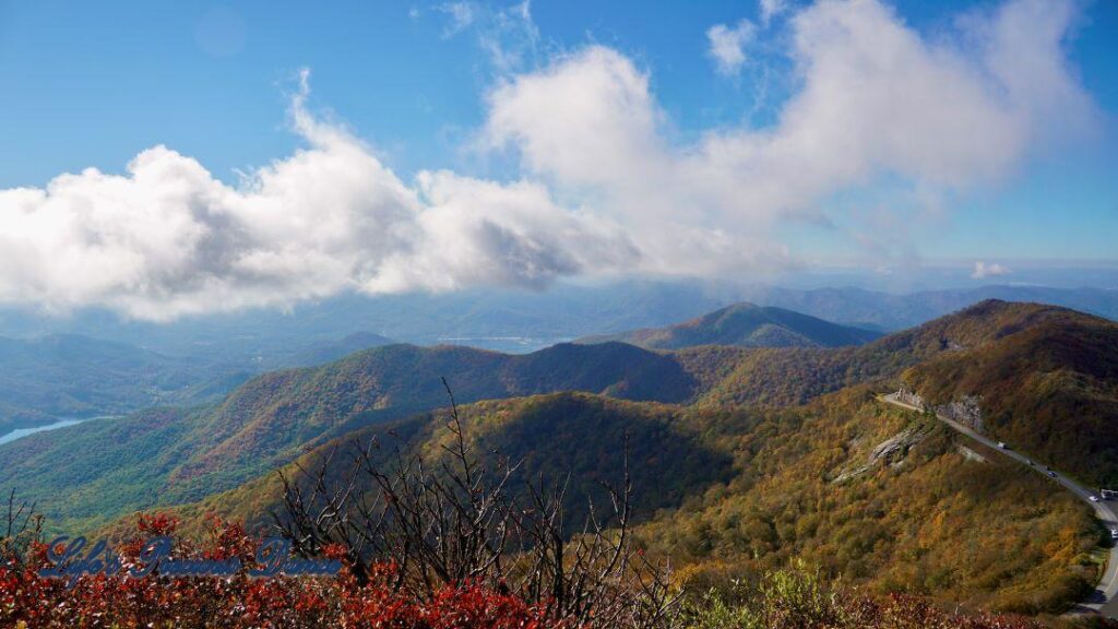 Landscape view of colorful trees, in the Blueridge mountains, surrounding a lake in the valley. Fluffy clouds above.