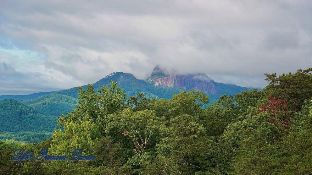 Landscape view of clouds surrounding the peak of Table Rock. Trees in the foreground.