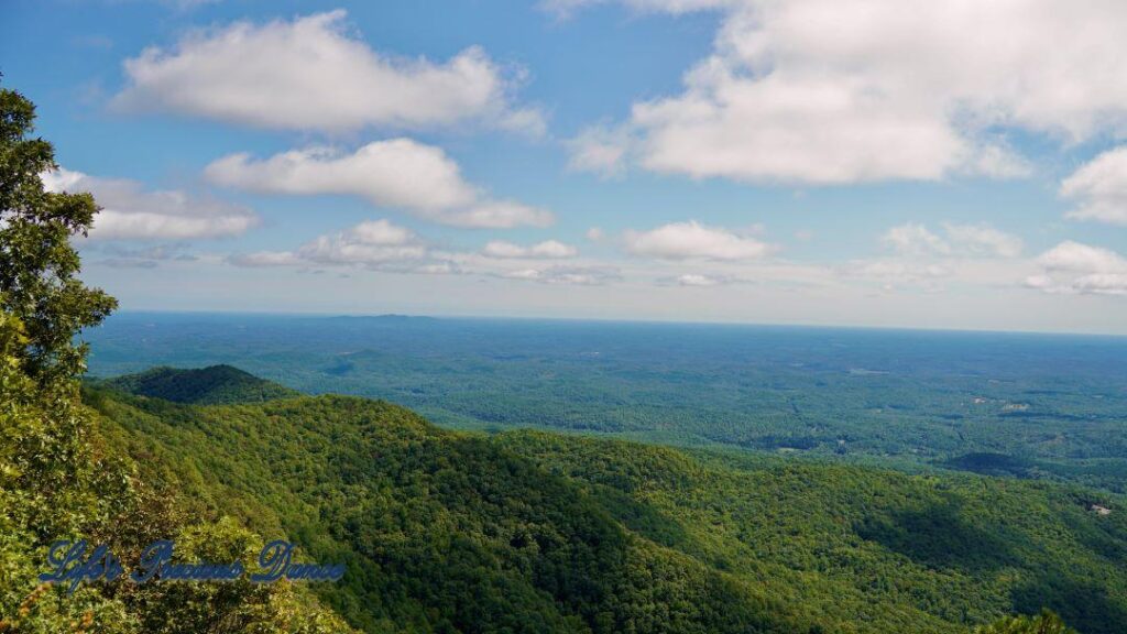 Landscape view of mountain ranges and a valley of forest. Clouds up above.