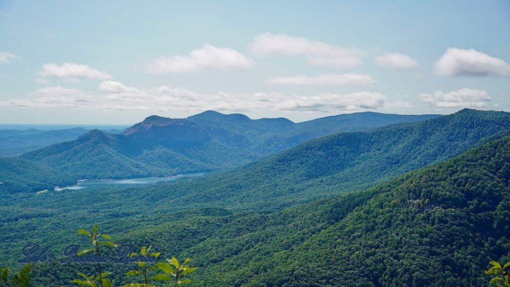 Landscape view of light fog covering mountain ranges, a lake and a valley of forest. Clouds up above.