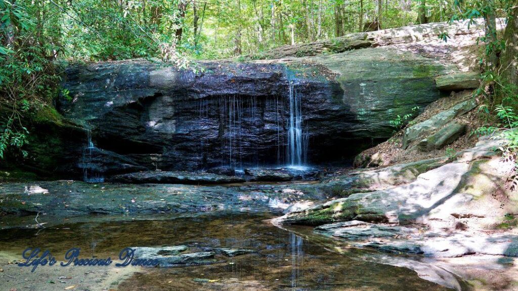 Waterfall spilling over a rock face into a mountain stream and reflecting in the water.