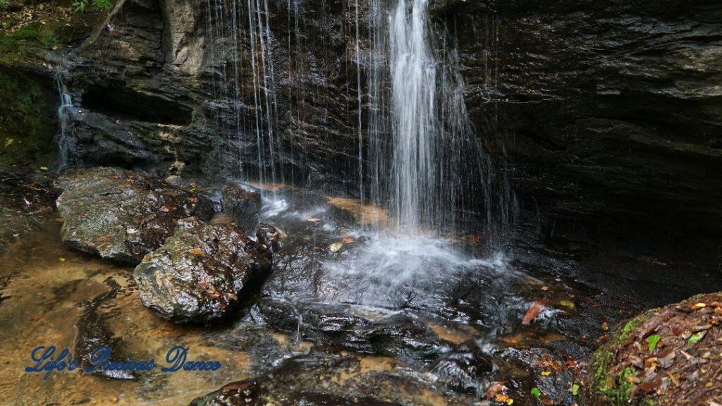 Waterfall spilling over a rock face into a mountain stream.