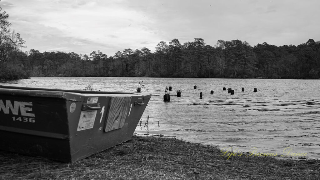 Black and white ground level view of a rowboat resting on the shore of Sesquicentennial Lake