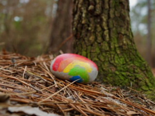 Rainbow colored painted rock at the base of a tree along a trail in Sesquicentennial State Park