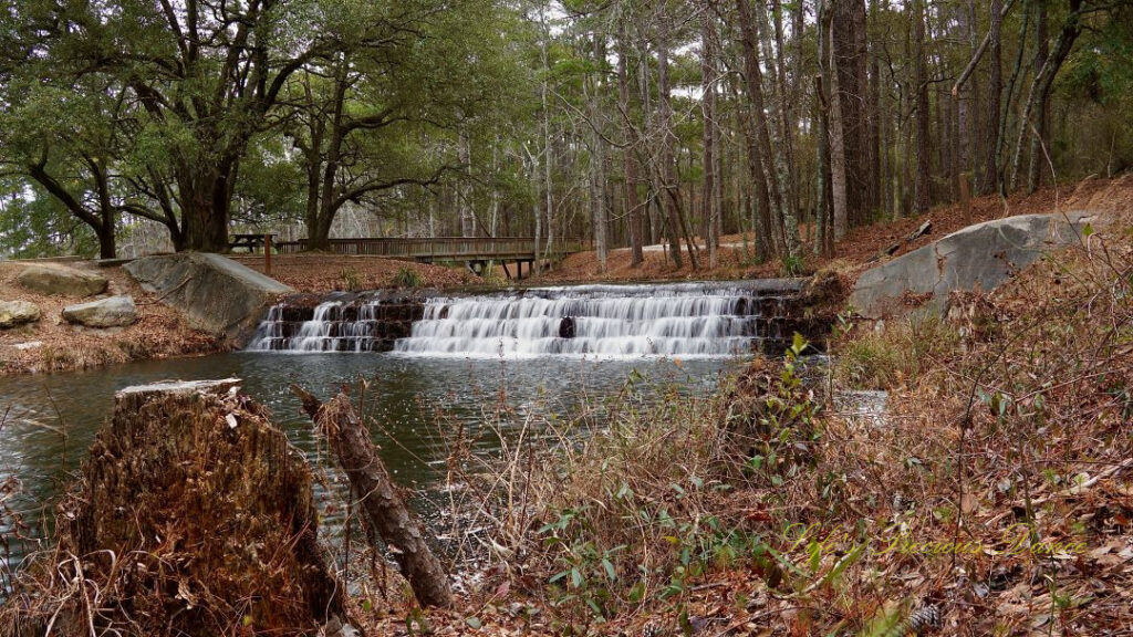 Upper section of the waterfall at Sesquicentennial State Park spilling into the creek. A pedestrian bridge in the background.