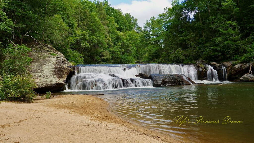 Riley Moore Falls spilling over rocks into the Chauga River. A sandy beach to the left.