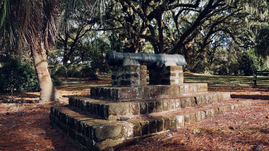 A replica cannon sits on a brick column. Angel oak trees in the background.