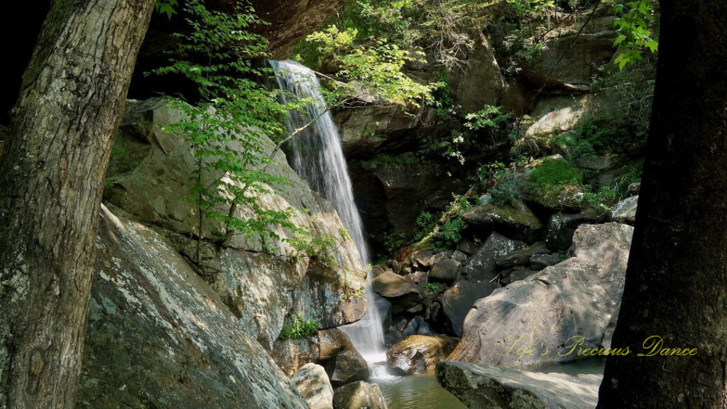 Eagle Falls spilling over a rockledge into a pool of water. A couple sits on a boulder in the foreground.