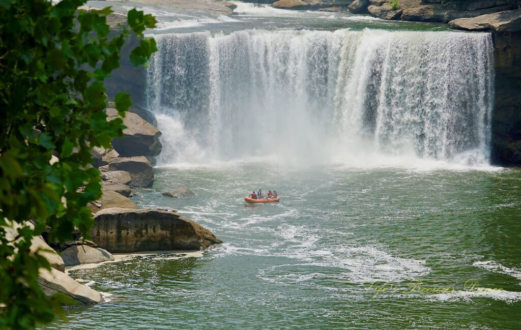 Landscape view of Cumberland Falls pouring over the rockface into the river. Rafters in the foreground.