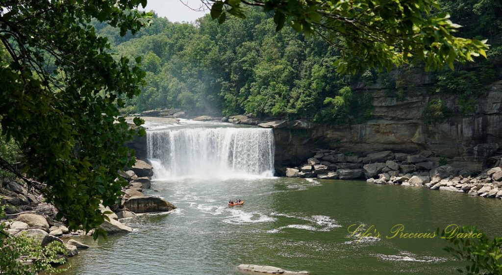 Landscape view of Cumberland Falls pouring over the rockface into the river. Rafters in the foreground.