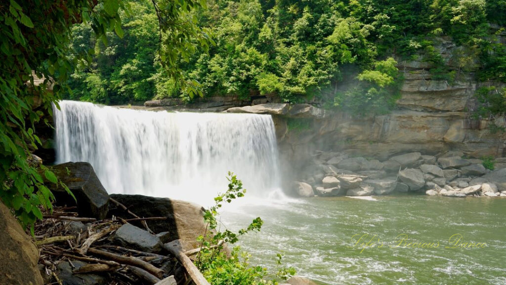 Cumberland Falls rapidly spilling into the river below. Trees and rockface mountains surrounding.