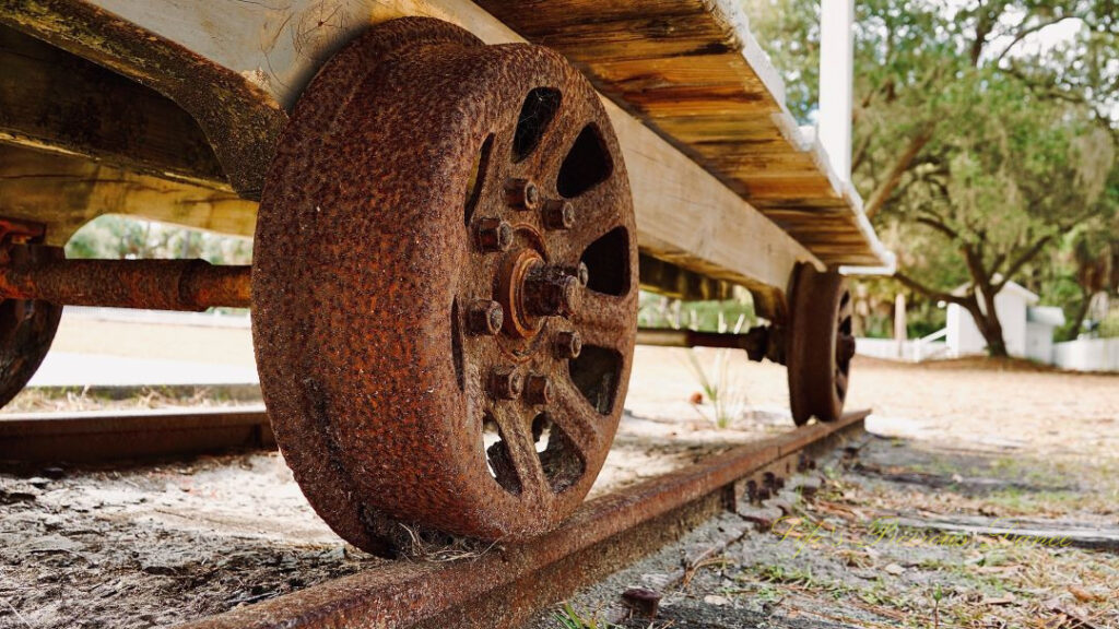 Looking upward from the ground at the rusted wheel of an old cart.