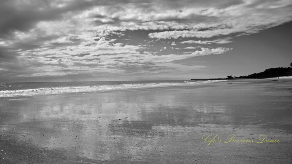 Black and white seascape view of the ocean, Waves rolling in and clouds reflecting on the beach.