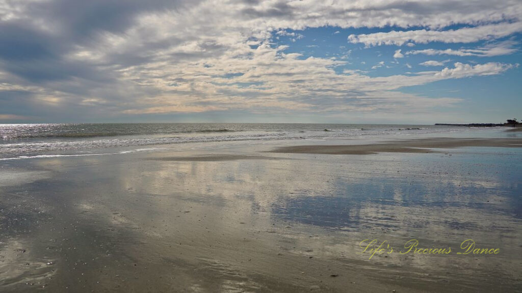 Seascape view of the ocean, Waves rolling in and blue skies and clouds reflecting on the beach.