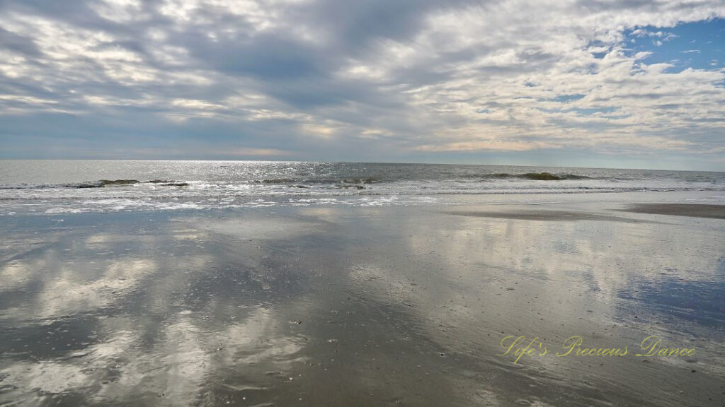 Seascape view of the ocean, Waves rolling in and blue skies and clouds reflecting on the beach.