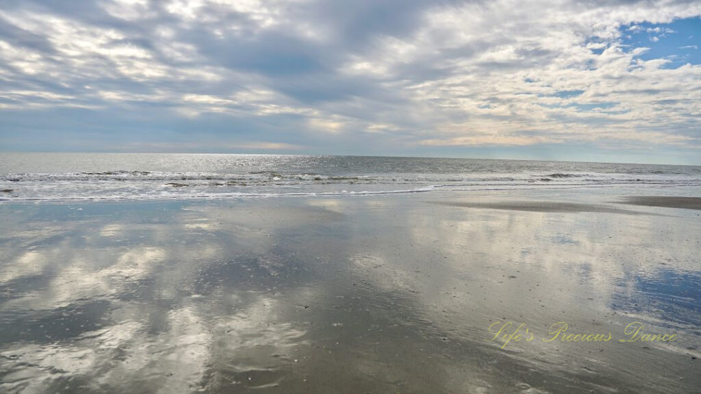 Seascape view of the ocean, Waves rolling in and blue skies and clouds reflecting on the beach.