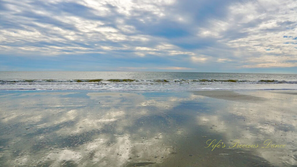 Seascape view of the ocean, Waves rolling in and blue skies and clouds reflecting on the beach.