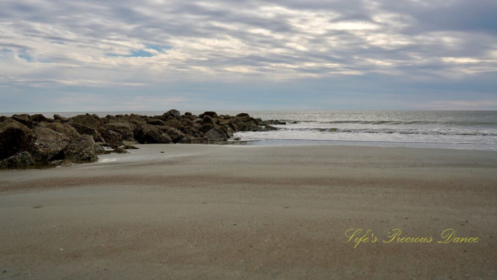 Side view of a rock barrier strewn across the beach leading out into the ocean.