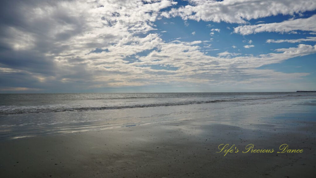 Seascape view of the ocean, Waves rolling in and a mix of dark and white fluffy clouds up above.