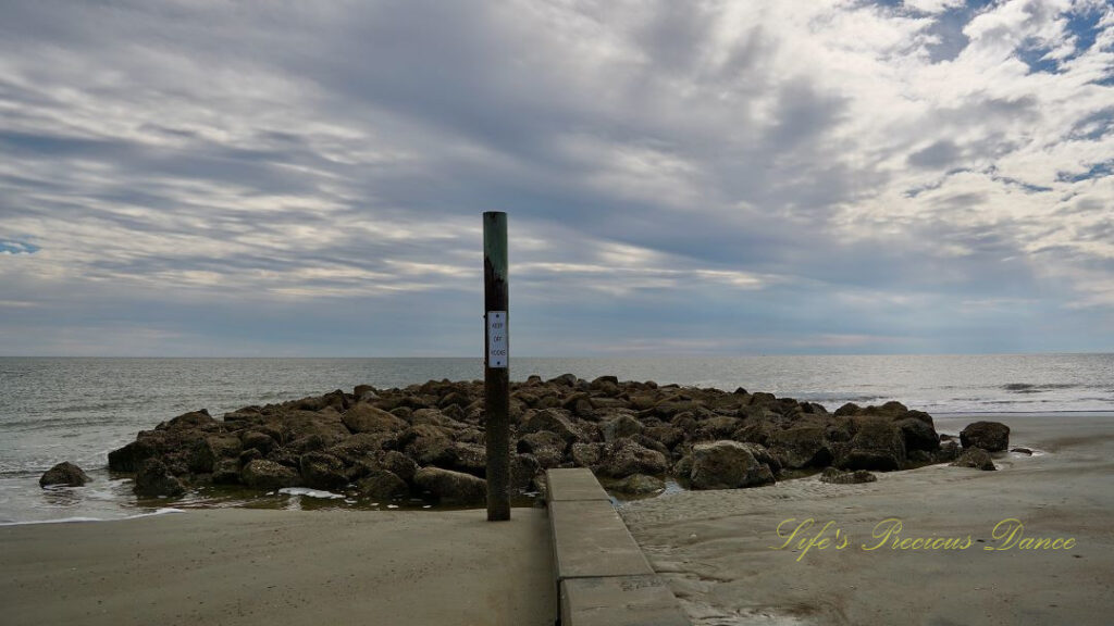 Sign post out front of rock barrier at Hunting Island beach. Ocean waves in the background.