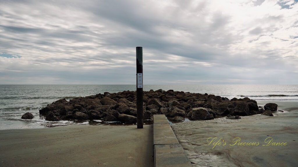 Sign post out front of rock barrier at Hunting Island beach. Ocean waves in the background.