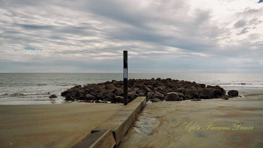 Sign post out front of rock barrier at Hunting Island beach. Ocean waves in the background.