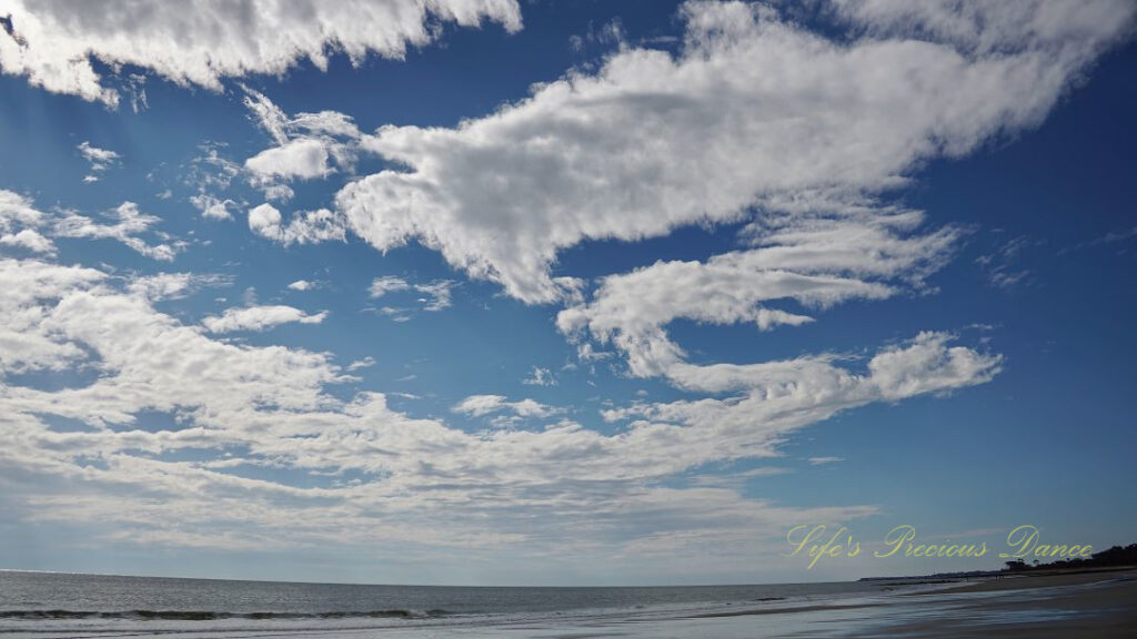 Curvy clouds, against a carolina blue sky, above the ocean.