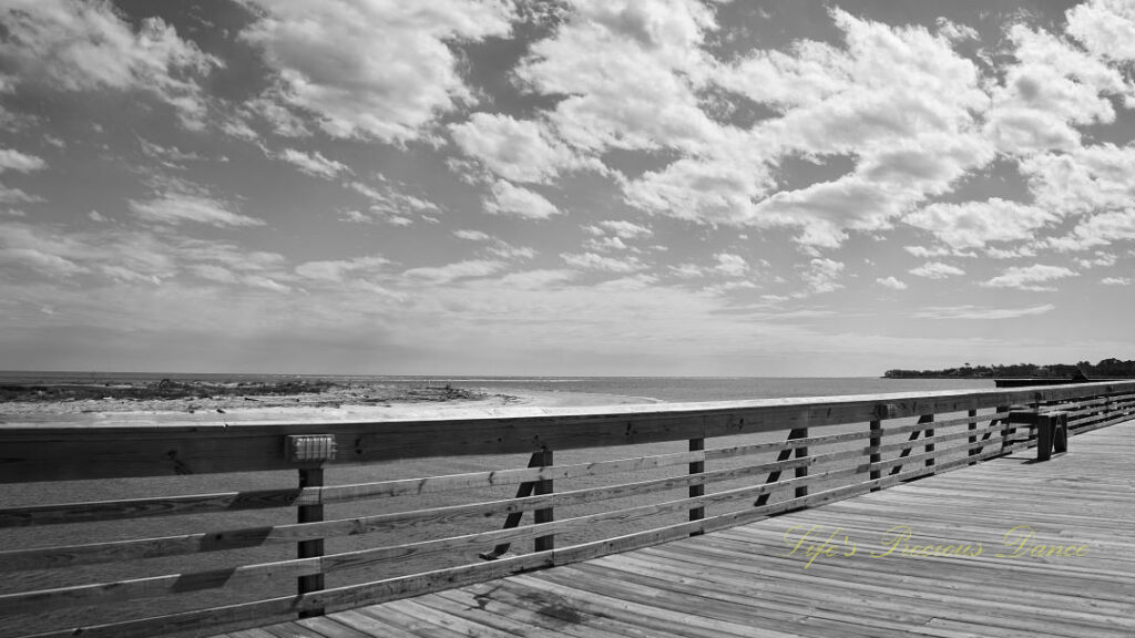 Black and white view of a pier and clouds above the atlantic ocean at Hunting Island State Park.