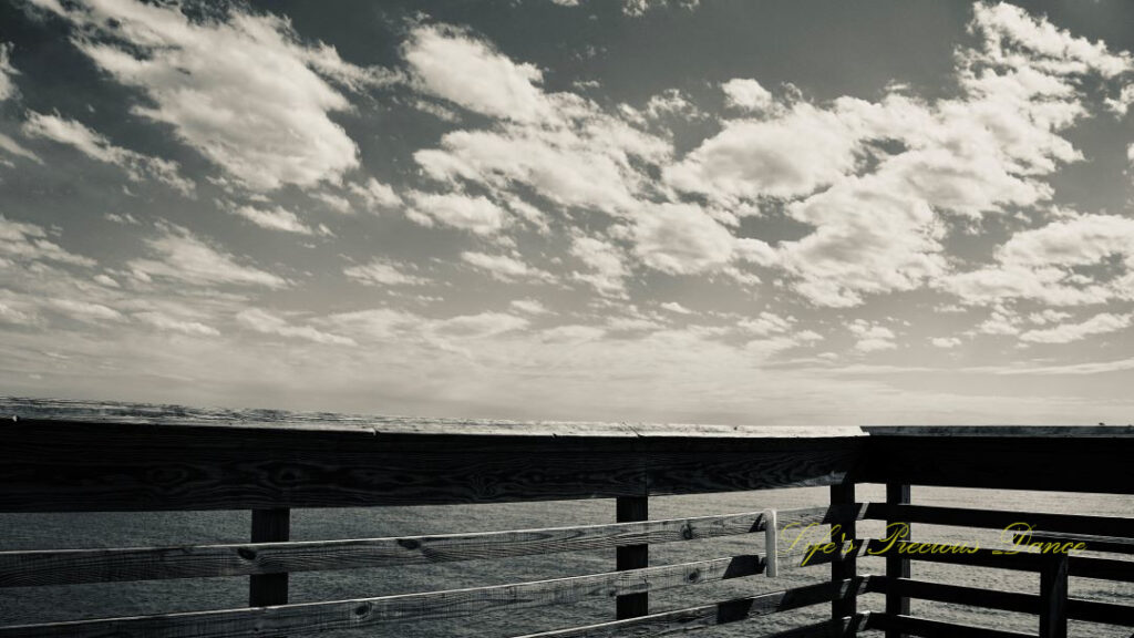 Black and white view of a pier and clouds above the atlantic ocean at Hunting Island State Park.