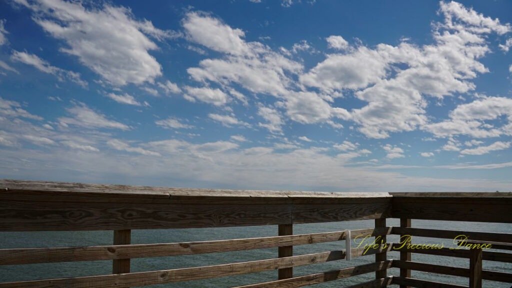 View from a pier overlooking the atlantic ocean at Hunting Island State Park. Fluffy clouds overhead.