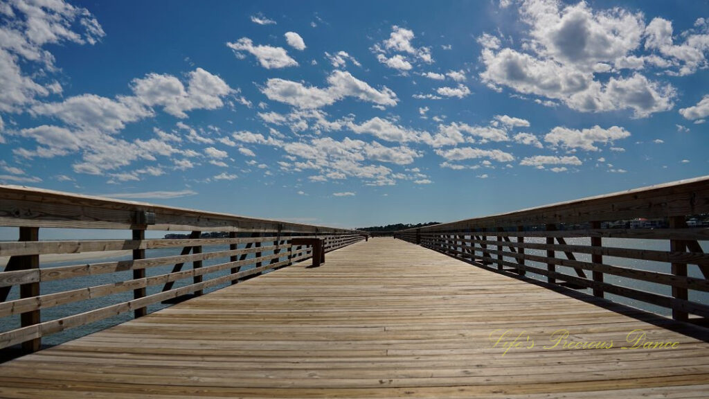 Ground level view of a fishing pier at Hunting Island State Park. Fluffy clouds up above.