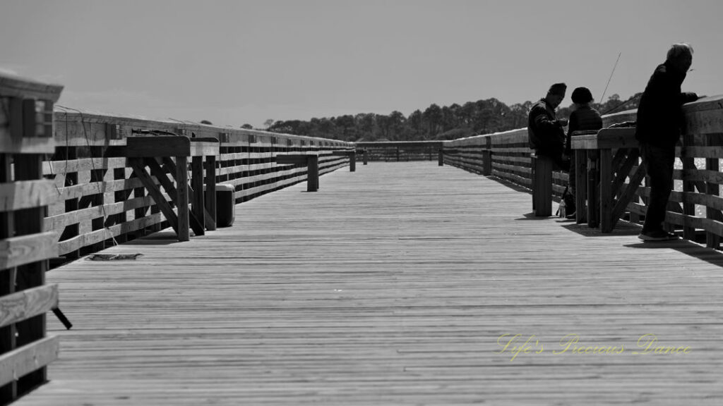 Black and white of three people fishing from a pier at Hunting Island State Park.