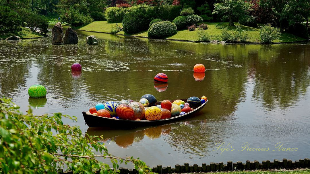 Colorful Chihuly glass art balls in a row boat and floating in a pond.