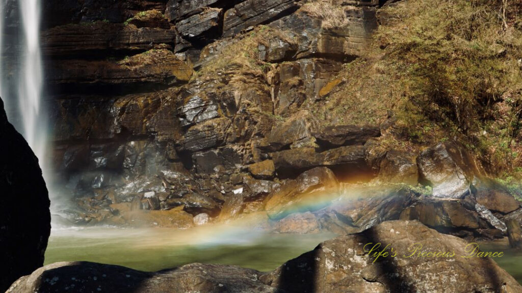 A rainbow reflecting in the mist above a pool of water as Toccoa Falls cascades down the rock face.