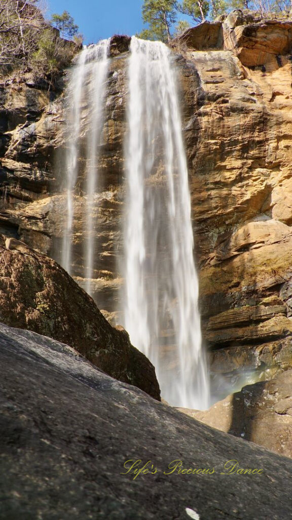 An 186 foot waterfall spilling over a rock face into a pool of water at Toccoa Falls. Boulders in the foreground.