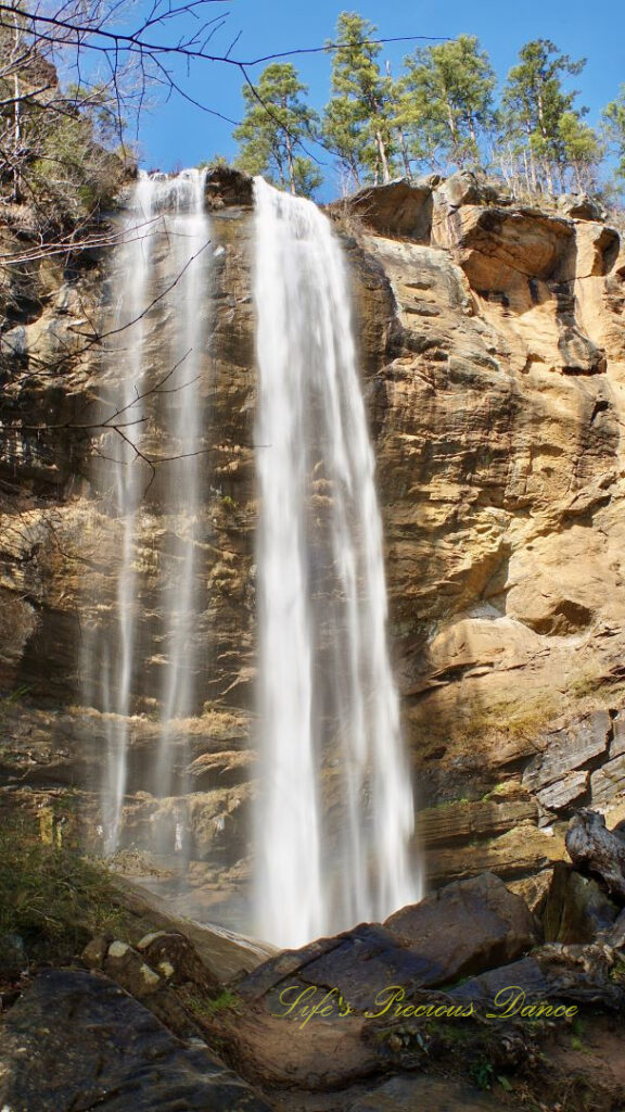 An 186 foot waterfall spilling over a rock face into a pool of water at Toccoa Falls. Boulders in the foreground.