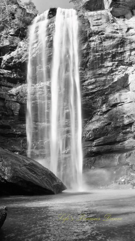 Black and white of an 186 foot waterfall spilling over a rock face into a pool of water at Toccoa Falls.