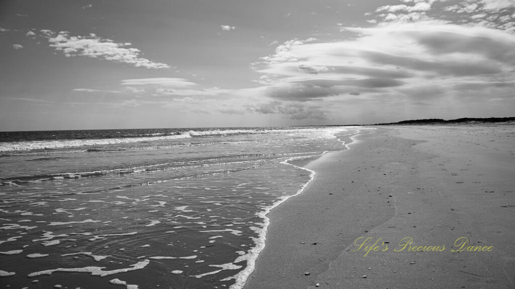 Black and white seascape view of Huntington Beach. Clouds above and waves crashing against the shore.