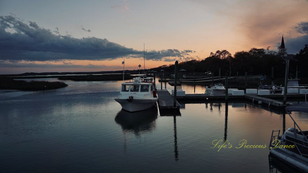 Boats along the dock and reflecting in the water at Murrells Inlet at dusk.