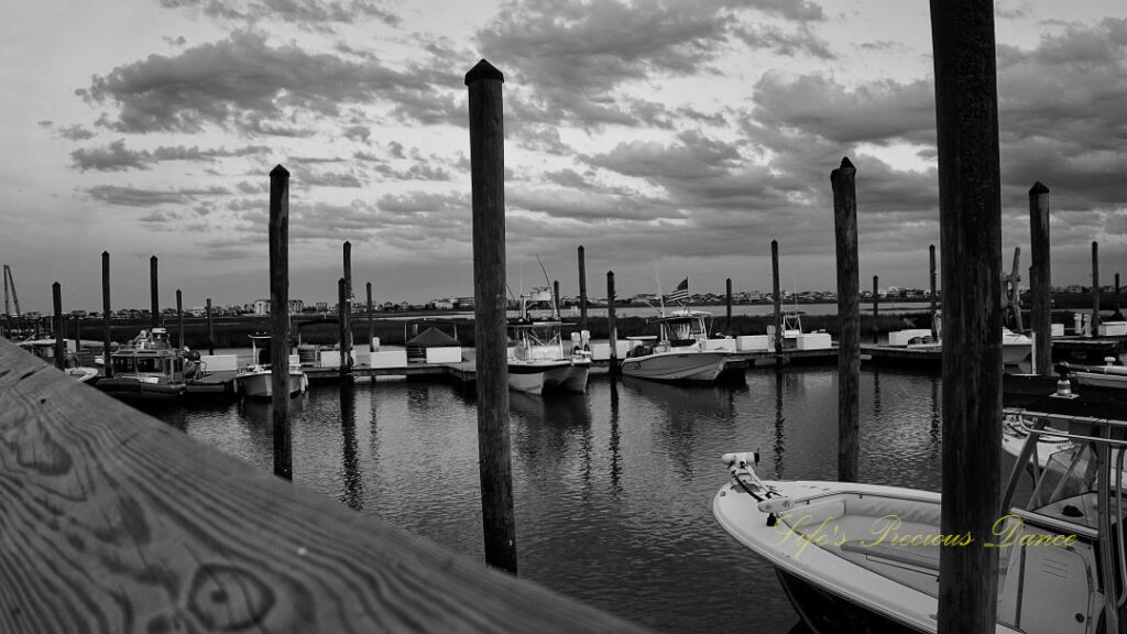 Black and white of boats along a dock at Murrells Inlet. Passing clouds overhead.