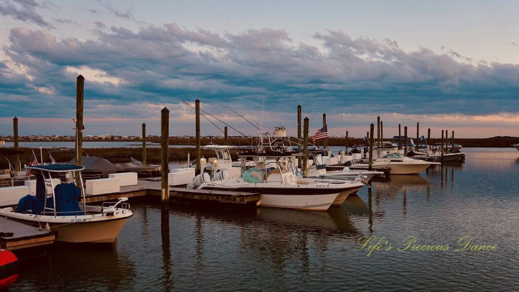 Boats lined up along a dock at Murrells Inlet and reflecting in the water. Passing clouds overhead.